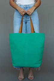 A person in light blue jeans and a white top holds the Panache Apparel Collection Green, Light Pink & Blue Western Tote, accessorized with gold rings and bracelets, standing against a plain gray background.