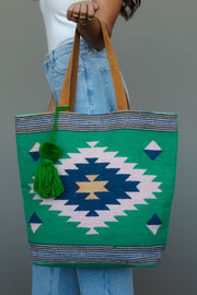 A person with long hair carries the Panache Apparel Collection Green, Light Pink & Blue Western Tote, featuring suede straps and a geometric pattern, while wearing blue jeans and a white sleeveless top.