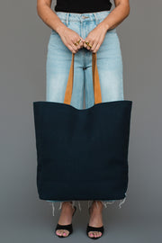 A person in light blue jeans and black heels holds the Panache Apparel Collection Mustard & Pink Drink At The Cabin Tote, standing against a plain gray background.