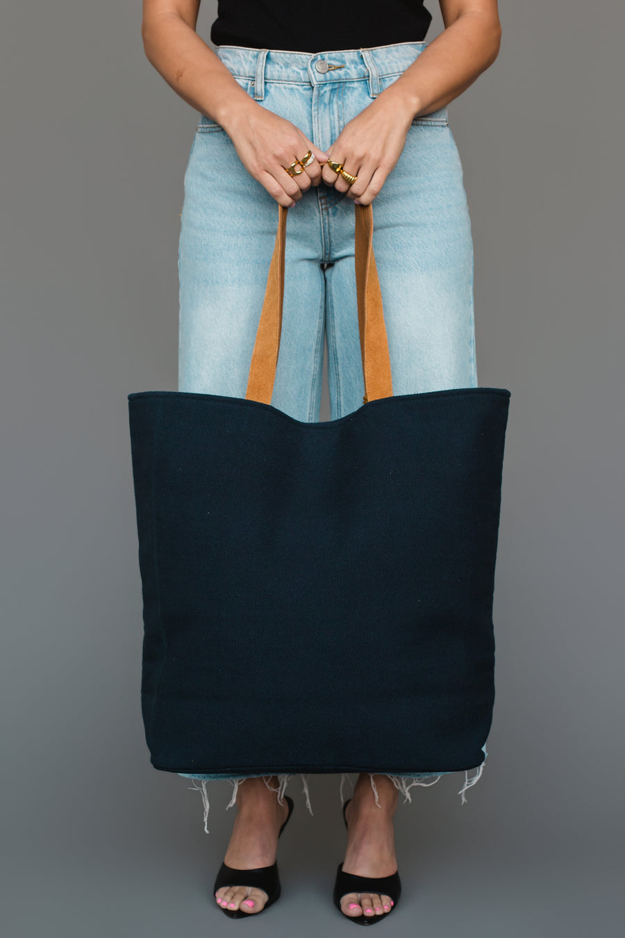 A person in light blue jeans and black heels holds the Panache Apparel Collection Mustard & Pink Drink At The Cabin Tote, standing against a plain gray background.