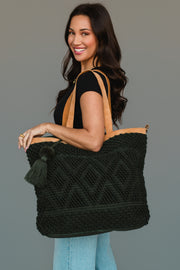 Smiling woman with long dark hair wearing a black shirt and light blue jeans, holding the Panache Apparel Collection Dark Green Diamond Pattern Textured Tote, which features camel-colored straps and a tassel, standing against a plain gray background.
