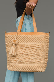 A person wearing a black shirt and blue jeans holds the panacheaccessories Tan Diamond Pattern Textured Tote, featuring a leather shoulder strap, against a plain gray background.