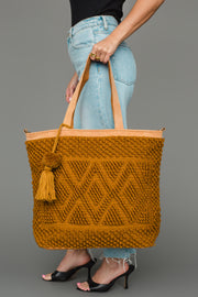 A person dressed in light blue jeans and black heels carries the Panache Apparel Collection Mustard Diamond Pattern Textured Tote, featuring a tassel detail and tan straps.