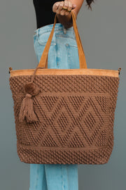 A person wearing blue jeans holds the Panache Apparel Collection Brown Diamond Pattern Textured Tote, featuring geometric patterns, leather handles, and a decorative tassel, against a plain gray background.