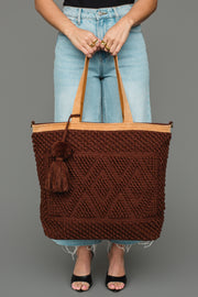 A person stands against a gray background, wearing light blue jeans and black heeled sandals, holding the Panache Apparel Collection Dark Brown Diamond Pattern Textured Tote featuring tan handles and a tassel.