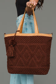 A person in jeans and a black top holds the Panache Apparel Collection’s Dark Brown Diamond Pattern Textured Tote, featuring leather handles and a tassel, against a plain gray background.