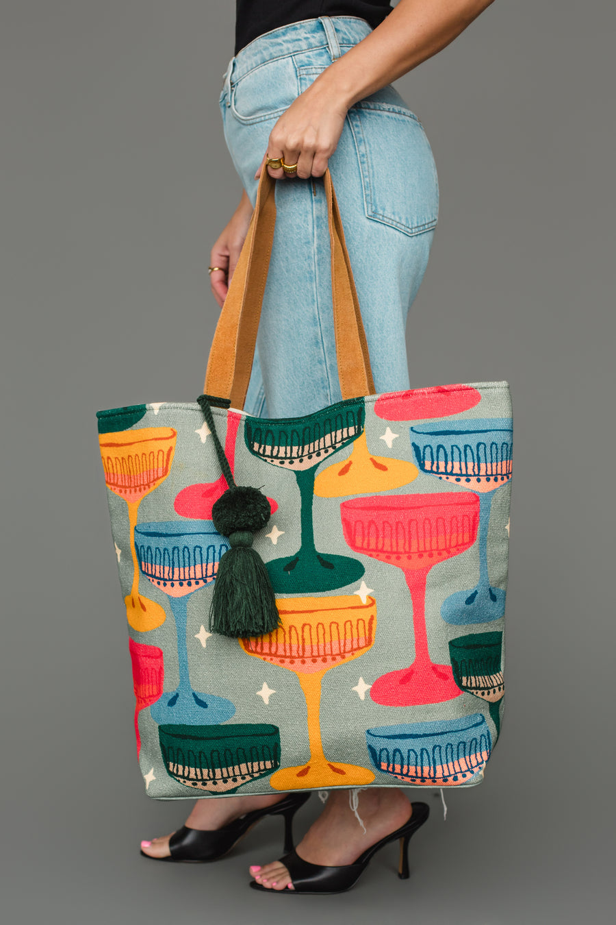 A person carries a Multicolored Coupe Glasses Tote featuring a pattern of coupe glasses and a hanging green tassel.