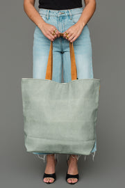 A person holding a spacious sage green Multicolored Coupe Glasses Tote with brown straps.