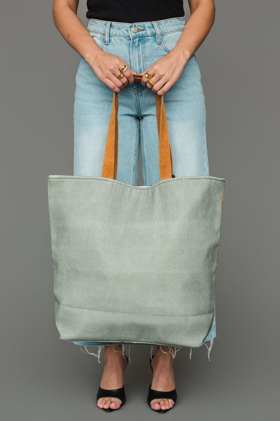 A person holding a spacious sage green Multicolored Coupe Glasses Tote with brown straps.