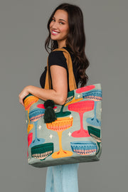 A woman carries a Multicolored Coupe Glasses Tote featuring a pattern of coupe glasses and a dark green tassel.