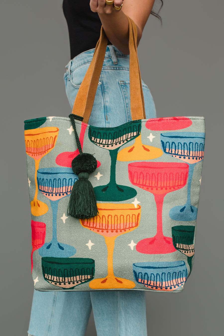 Multicoloured Coupe Glasses Tote featuring a multicolored coupe glass print and a dark green tassel hanging from the strap.