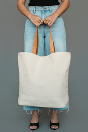A person in light blue jeans and black heels holds the Panache Apparel Collection White, Gray & Camel Western Tote in front of a gray background. Only their torso and legs are visible.