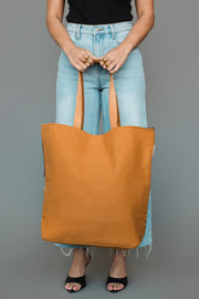 A person in a black top, light blue jeans, and black heels holds the Camel, Brown & Cream Western Tote by Panache Apparel Collection with both hands. The image focuses on the tote and the lower part of the person’s body.
