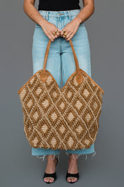 A person in light blue jeans and black sandals holds the Panache Apparel Collection Brown & Cream Diamond Pattern Textured Tote, standing against a plain gray background.
