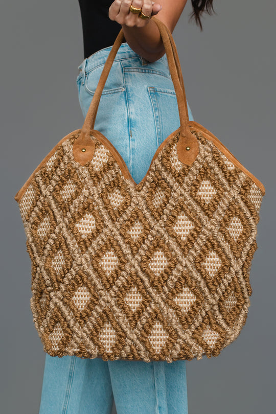 A person in blue jeans holds the Panache Apparel Collection Brown & Cream Diamond Pattern Textured Tote, featuring tan handles, against a plain gray background.