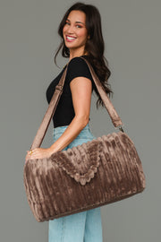 A woman in a black top and jeans smiles while holding the Panache Apparel Collection Brown Super Soft Ribbed Duffel, featuring a shoulder strap, against a plain gray background.