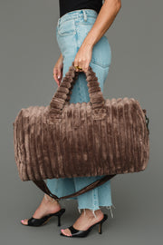A person wearing light blue jeans and black heels holds the Panache Apparel Collection Brown Super Soft Ribbed Duffel with both hands against a plain gray background.