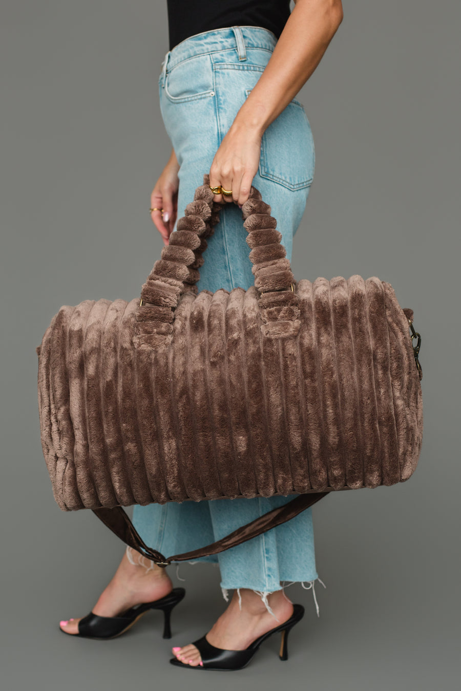 A person wearing light blue jeans and black heels holds the Panache Apparel Collection Brown Super Soft Ribbed Duffel with both hands against a plain gray background.