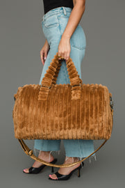 A person in blue jeans and black heels holds the Mustard Super Soft Ribbed Duffel from Panache Apparel Collection, featuring matching handles and a detachable shoulder strap, standing against a plain gray background.