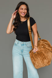 A smiling woman with long dark hair wears a black top and light blue jeans, carrying the Panache Apparel Collection Mustard Super Soft Ribbed Duffel over her shoulder, standing against a plain gray background.