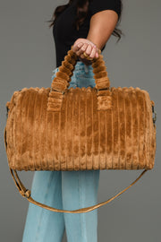 A person in a black top and blue jeans holds the Mustard Super Soft Ribbed Duffel by Panache Apparel Collection, featuring a shoulder strap and ruffled handles, against a plain gray background.