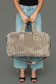 A person in frayed light blue jeans and black heels holds the Panache Apparel Collection Gray Super Soft Ribbed Duffel, featuring short handles and a removable shoulder strap, against a plain gray background.