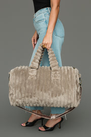 A person wearing blue jeans and black heels holds the Panache Apparel Collection Gray Super Soft Ribbed Duffel, featuring matching handles and a shoulder strap, against a gray background.