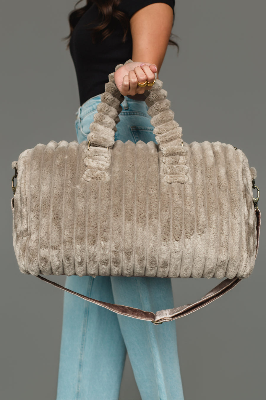 A person wearing a black shirt and blue jeans holds the Panache Apparel Collection Gray Super Soft Ribbed Duffel, featuring round handles and a shoulder strap, against a gray background.