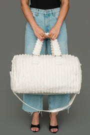 A person in jeans and black sandals holds the Panache Apparel Collection Cream Super Soft Ribbed Duffel, featuring textured handles, against a plain gray background.