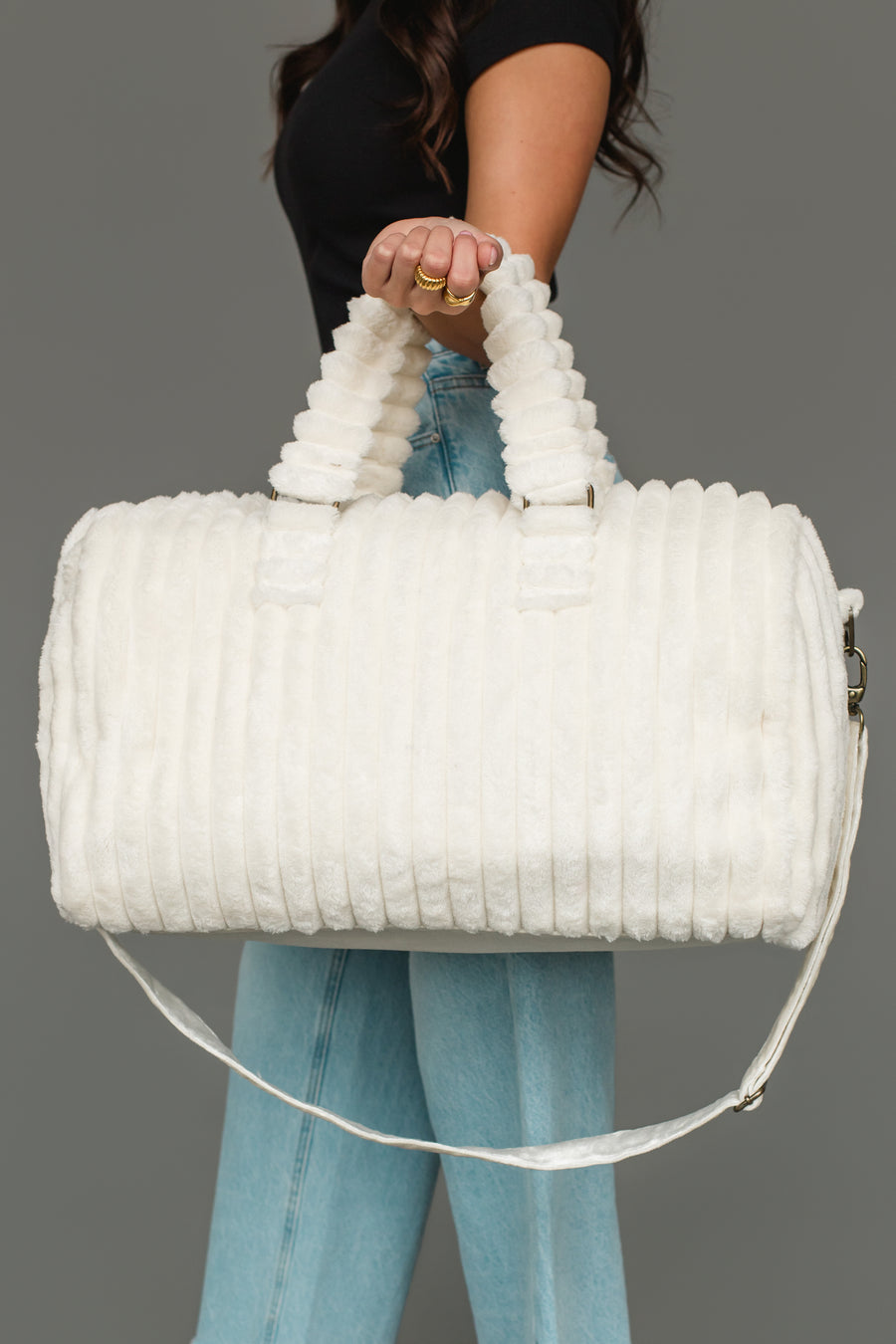 A person in a black top and blue jeans holds the Panache Apparel Collection Cream Super Soft Ribbed Duffel, with short handles and a long shoulder strap, against a plain gray background.