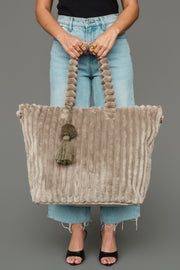 A person in jeans and a black top holds the Panache Apparel Collection Gray Super Soft Ribbed Tote, featuring thick handles and tassel accents, while standing against a plain gray background.