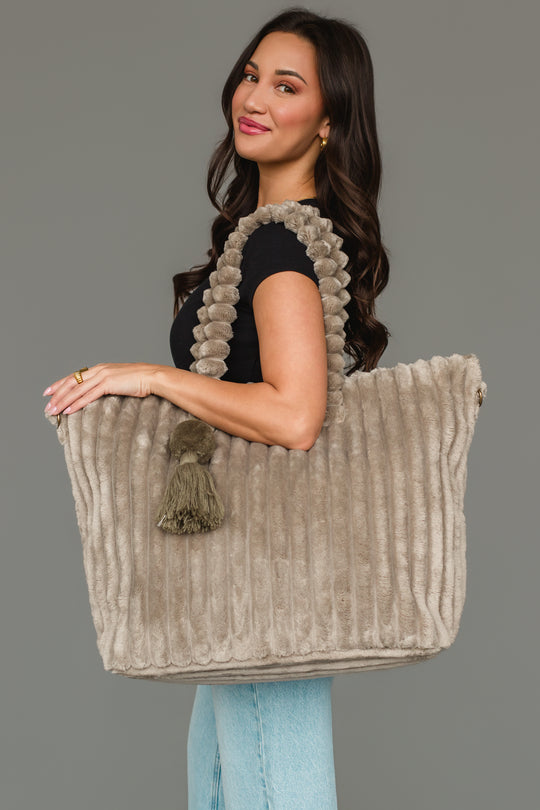 A woman in a black top and blue jeans holds the Panache Apparel Collection’s Gray Super Soft Ribbed Tote, featuring textured handles and a tassel, standing against a plain gray background.
