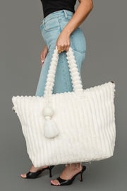 A person in jeans and heels holds the Panache Apparel Collection’s Cream Super Soft Ribbed Tote, featuring a large rounded handle and tassel, against a plain gray background.