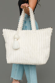 A woman wearing a black top and blue jeans holds the Panache Apparel Collection Cream Super Soft Ribbed Tote, featuring twisted handles and decorative tassels, against a plain gray background.