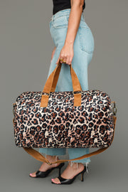A person in jeans and black heels holds the Panache Apparel Collection Brown & Cream Leopard Duffel against a plain gray background.