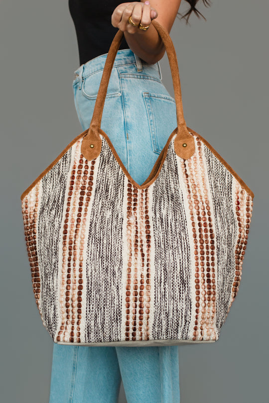 A woman in light blue jeans and a black top holds the Panache Apparel Collection Gray & Brown Textured Tote, featuring brown handles and accents, against a plain gray background.