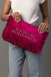A person in a white sleeveless top and jeans holds the You’re Like Really Pretty Ruffle Travel Pouch by Panache Apparel Collection, a pink velvet clutch with ruffled edges and the words “YOU’RE LIKE REALLY PRETTY” embroidered in white letters.