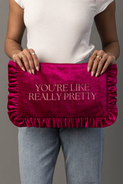 A person in a white top and jeans holds a large, ruffled hot pink clutch with the words YOURE LIKE REALLY PRETTY embroidered on it in white letters.