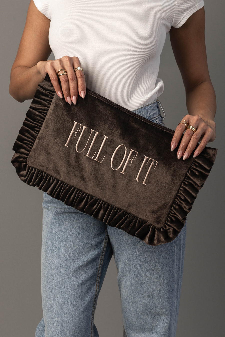 A person in a white top and jeans holds the Panache Apparel Collection Full Of It Ruffle Travel Pouch, featuring “FULL OF IT” embroidered on the front.