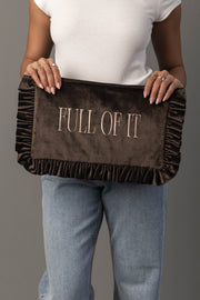 A person wearing a white shirt and blue jeans holds the Full Of It Ruffle Travel Pouch by Panache Apparel Collection, a brown velvet clutch with ruffled edges and “FULL OF IT” embroidered on the front.