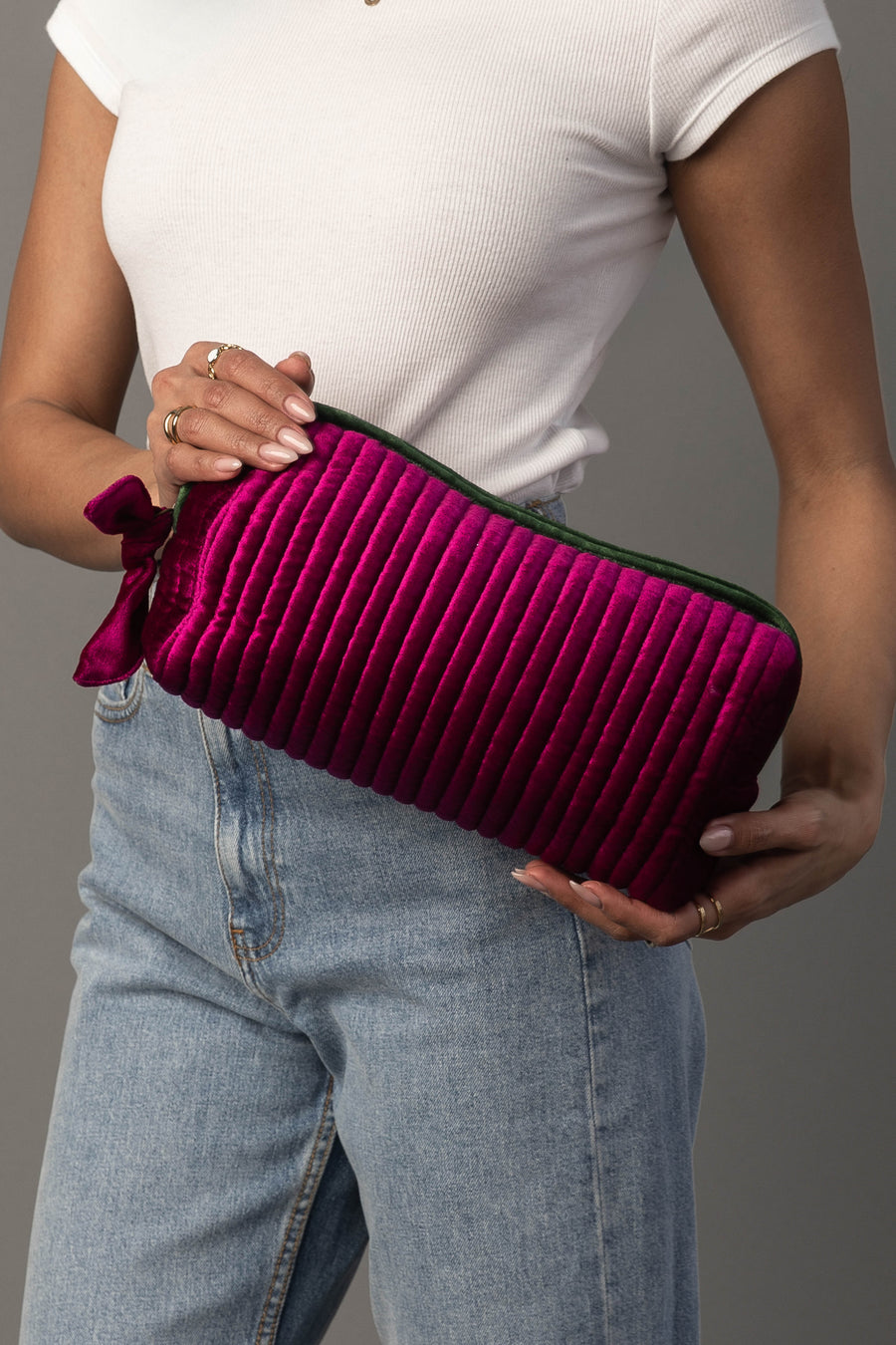 A person in a white shirt and blue jeans holds the Panache Apparel Collection Fuchsia & Green Ribbed Travel Pouch against a gray background.