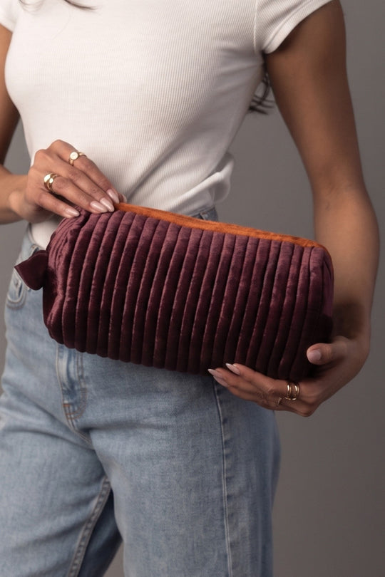 A woman in a white top and jeans holds the Purple & Orange Ribbed Travel Pouch by Panache Apparel Collection, a zippered pouch featuring orange lining.