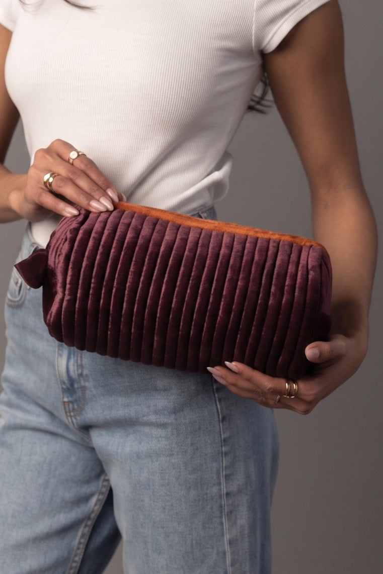A woman in a white top and jeans holds the Purple & Orange Ribbed Travel Pouch by Panache Apparel Collection, a zippered pouch featuring orange lining.