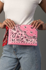 A person wearing a white shirt and blue jeans holds the Pink Bandana Clutch from Panache Apparel Collection. They have several rings on their fingers and a red bandana tied to their belt loop.