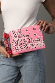 A person dressed in blue jeans and a white top holds the Panache Apparel Collection Pink Bandana Clutch. A red bandana is tied around their jean belt loop, set against a gray background.