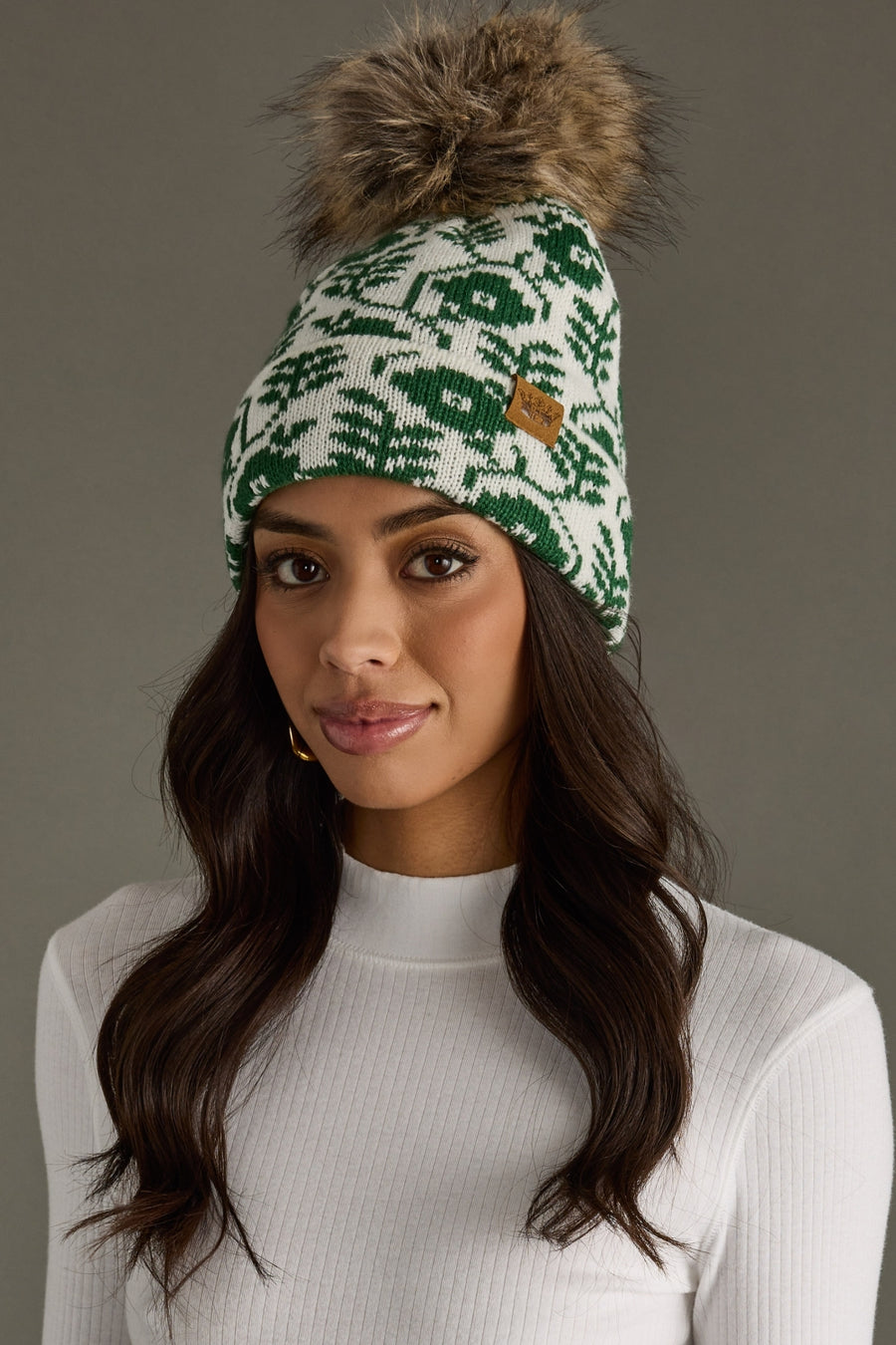 Woman wearing a green patterned beanie with a fur pom-pom on a gray background