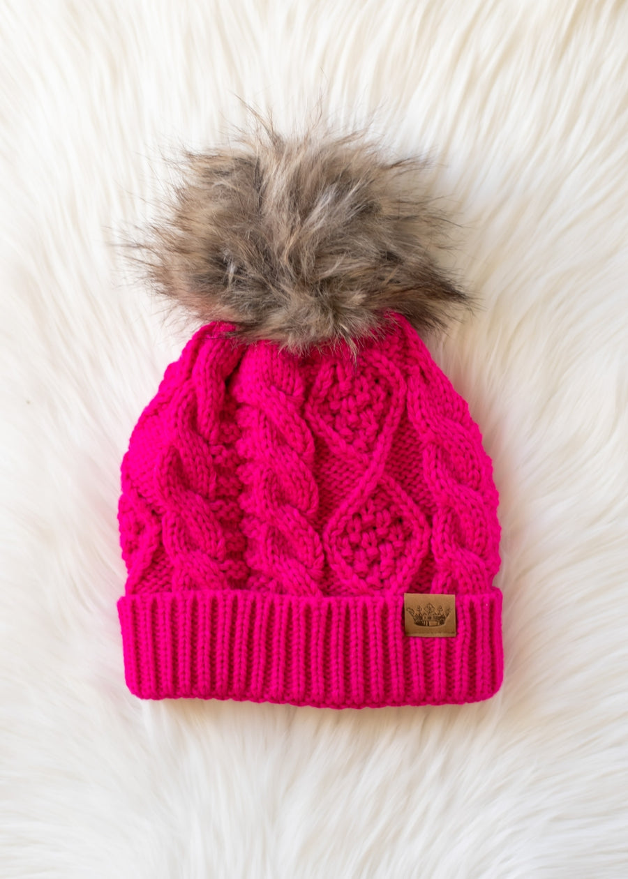 Pink knit beanie with fur pom-pom on a white fluffy background