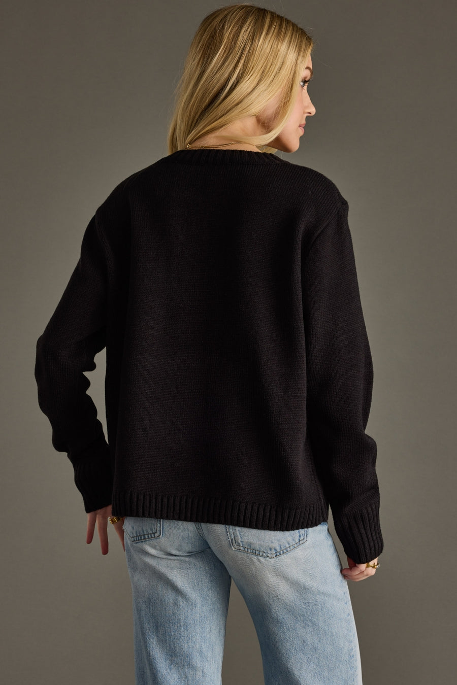 Person wearing a black sweater and light blue jeans against a gray background