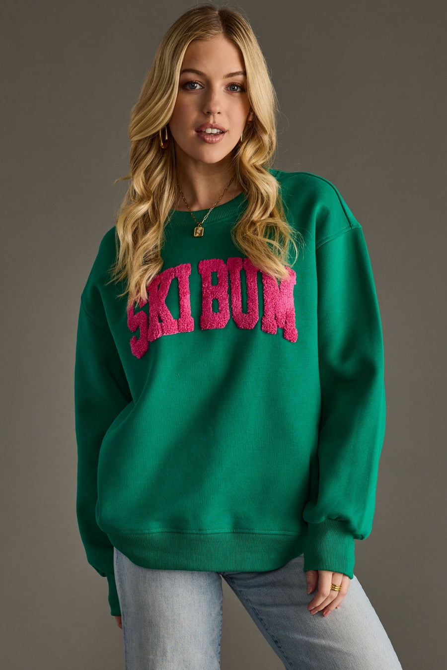 Woman wearing a green sweatshirt with pink text on a gray background