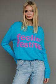 Woman wearing a blue sweater with 'feelin' festive' text against a gray background